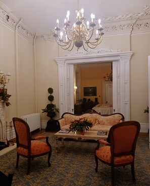 Una sala de estar formal con un sofá, dos sillones, una araña y una chimenea.