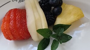 Une assiette contenant des fraises, des bananes, des myrtilles, de l’ananas et des feuilles de menthe.