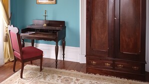 Une pièce aux murs de couleur turquoise, avec un meuble en bois, un bureau avec une lampe, une chaise et un tableau encadré accroché au mur.
