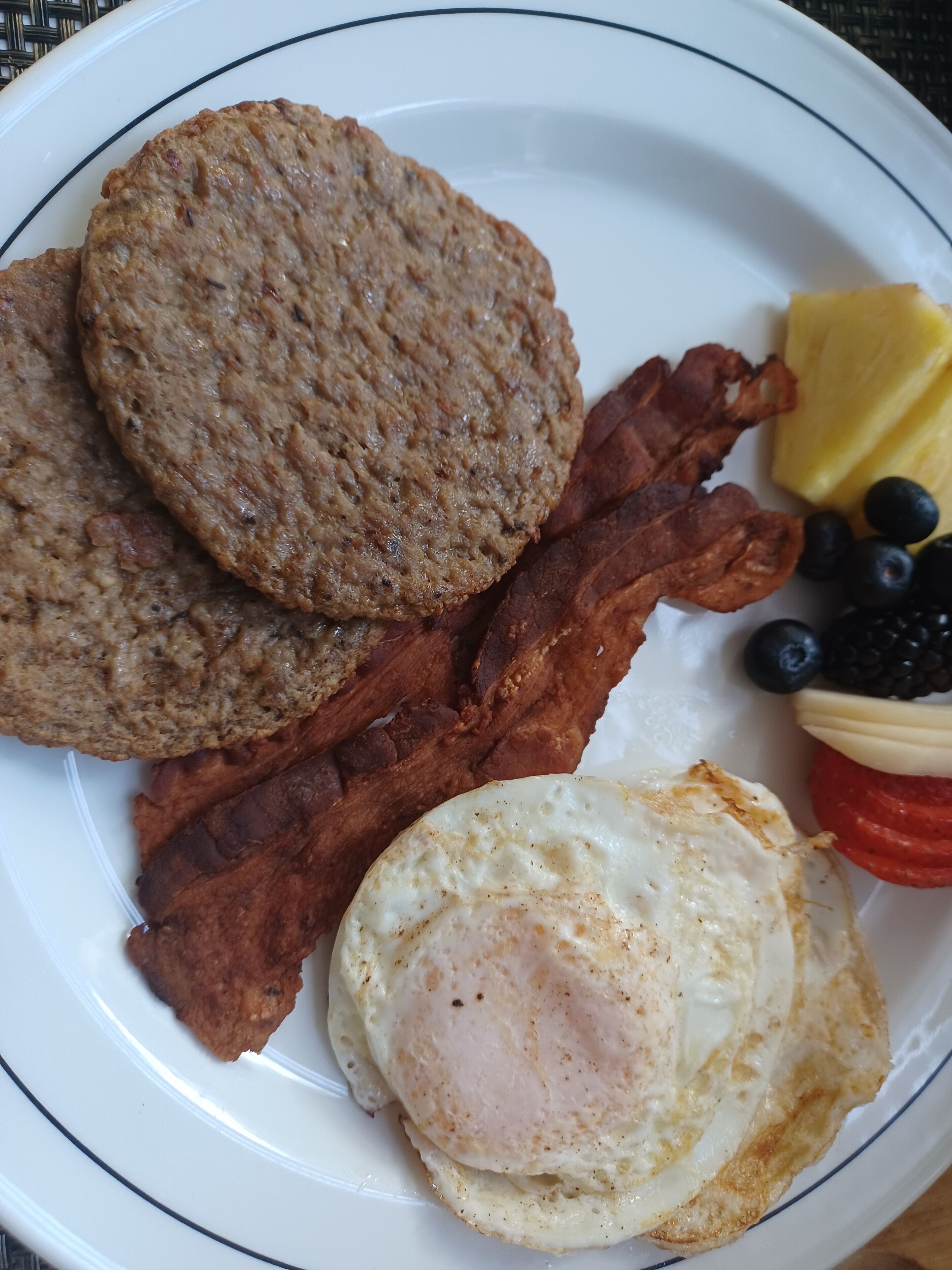 Um prato com bacon, ovos e uma fatia de abacaxi.