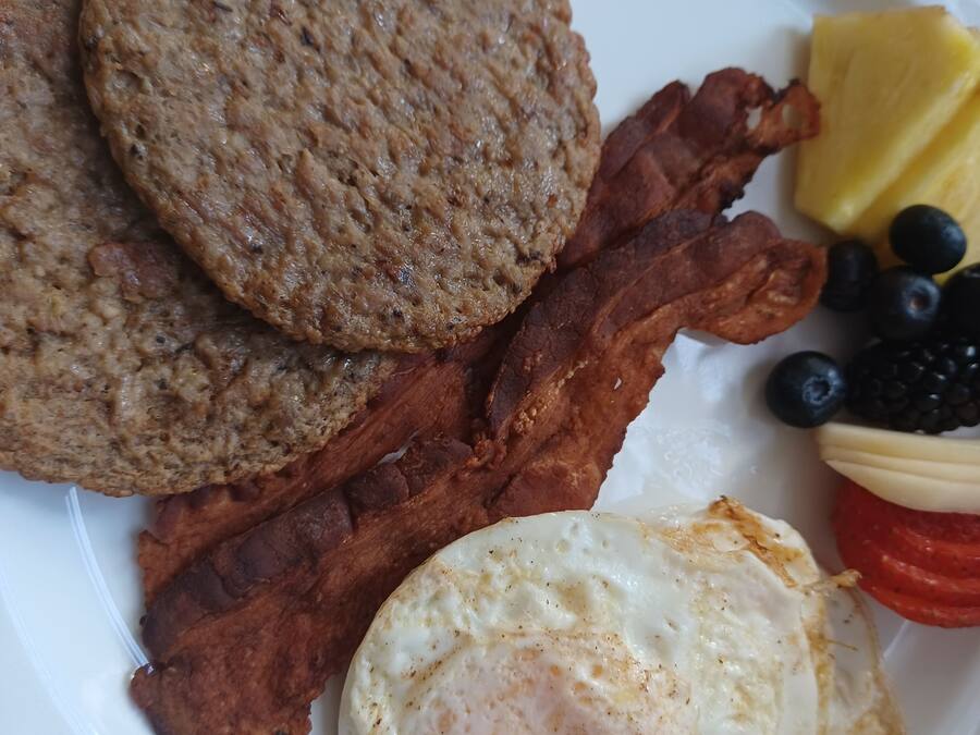 Um prato com bacon, ovos e uma fatia de abacaxi.