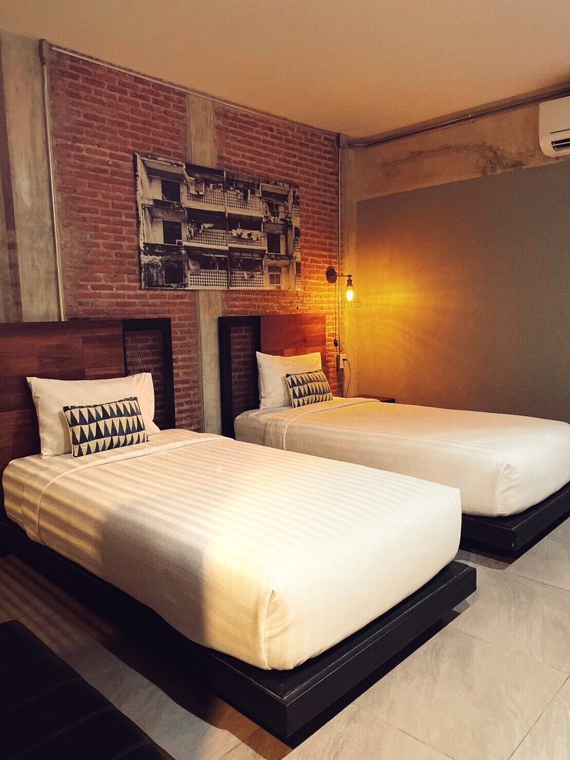 A hotel room with two beds, a brick wall, and a modern light fixture.