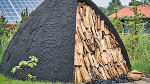 Estructura en forma de domo geodésico con exterior negro y un interior visible repleto de troncos apilados.