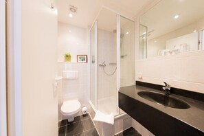 A modern bathroom with a glass-enclosed shower, a black sink, and a white toilet.