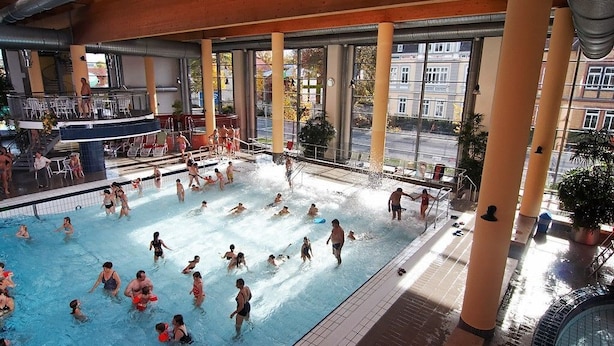 Una gran piscina interior con múltiples carriles, rodeada de amplias ventanas y columnas.