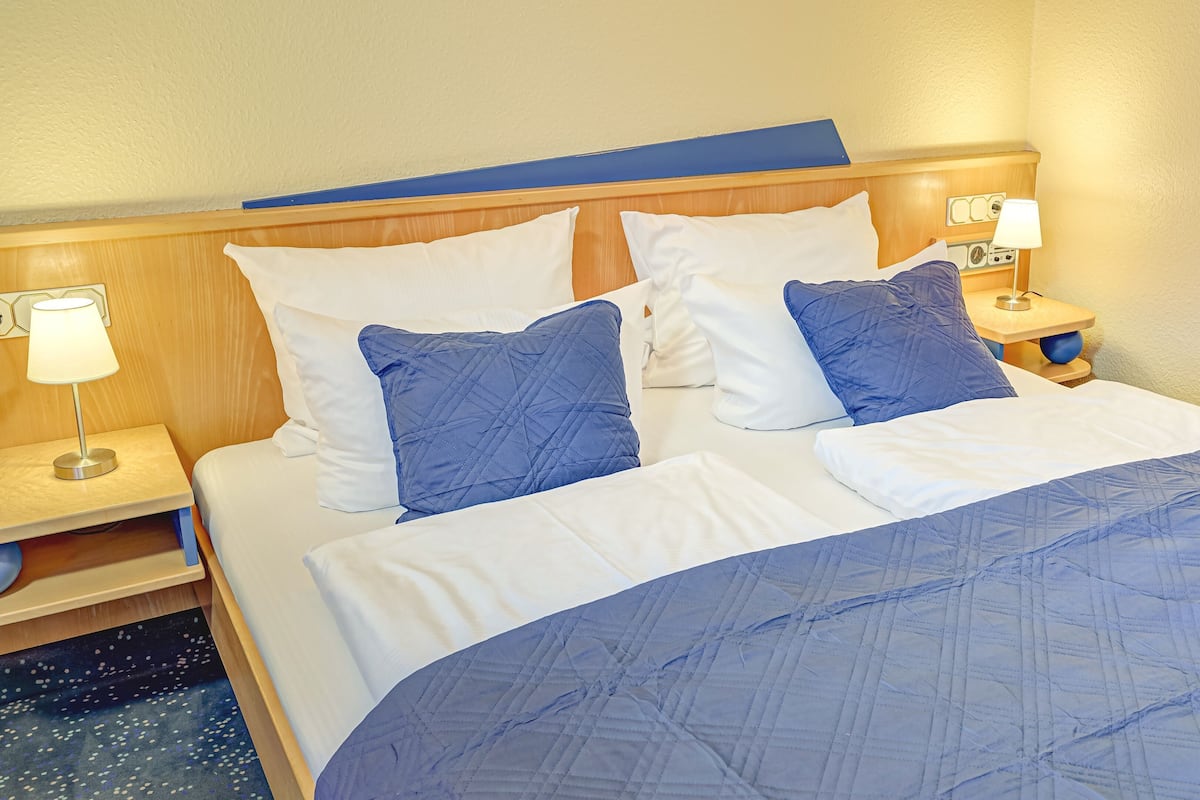 A hotel room with a bed, two bedside tables with lamps, and a wooden headboard.