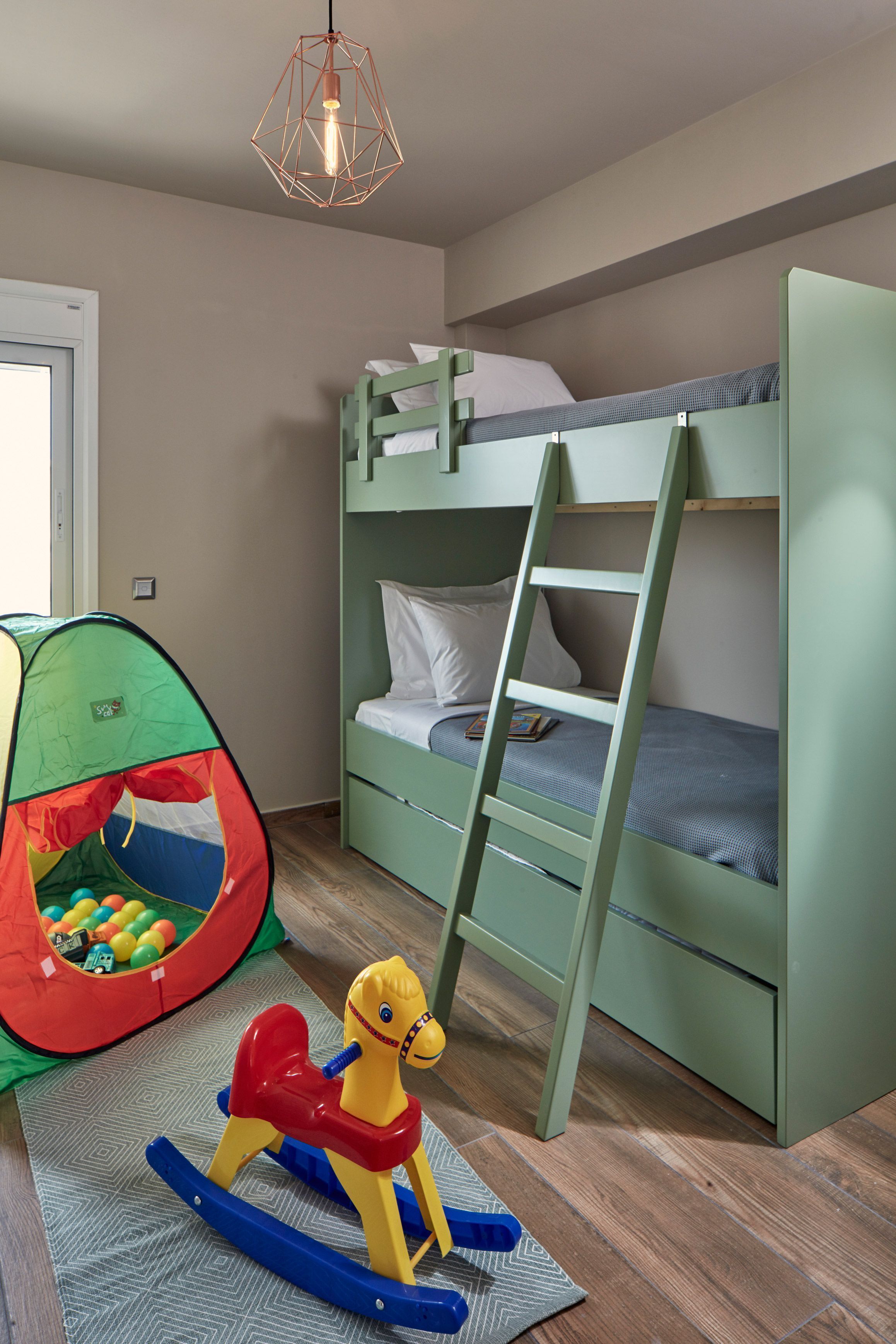A bunk bed with a ladder, a play tent, and a rocking horse in a room with wooden flooring.