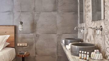 A modern bathroom with a large round sink, a mirror, and a wooden bedside table with books and toiletries.
