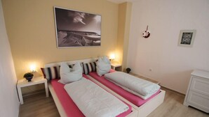 A double bed with white and pink bedding, two bedside tables with lamps, a wall-mounted picture, and a small plant on one table. - Ferienwohnung Backstube König (Brandenburg an der Havel)