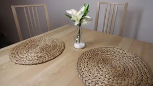 A wooden table with woven placemats and a vase with white flowers. - Ferienwohnung Backstube König (Brandenburg an der Havel)