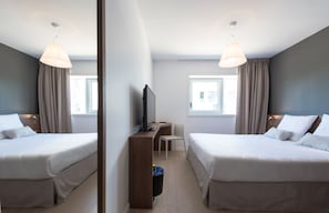 Quarto de hotel com duas camas, uma escrivaninha, uma cadeira, uma televisão e uma janela.