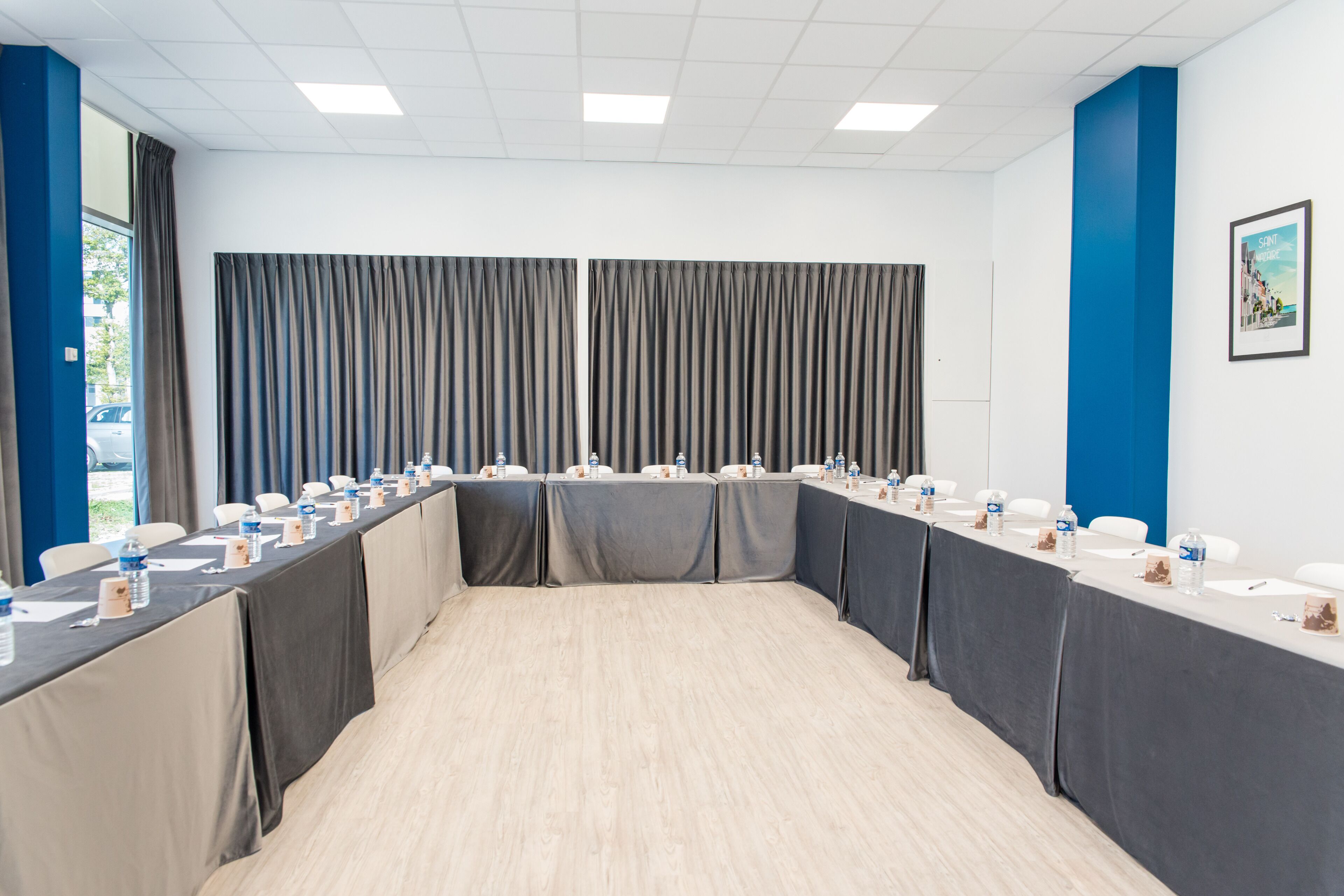 Uma sala de conferência com uma mesa comprida, cadeiras e um painel de cortina.