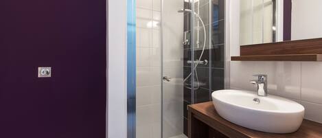 Un baño moderno con cabina de ducha de vidrio, lavamanos blanco y tocador de madera.