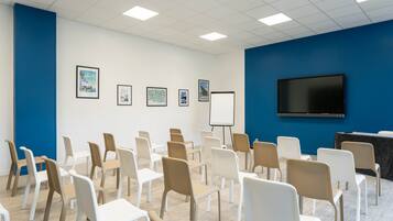 A conference room with rows of chairs, a whiteboard, and a television on the wall.