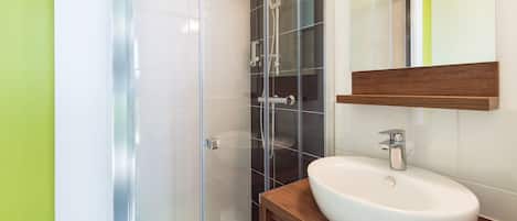 Un bany modern amb un envà de dutxa de vidre, un lavabo blanc i un moble de tocador de fusta.
