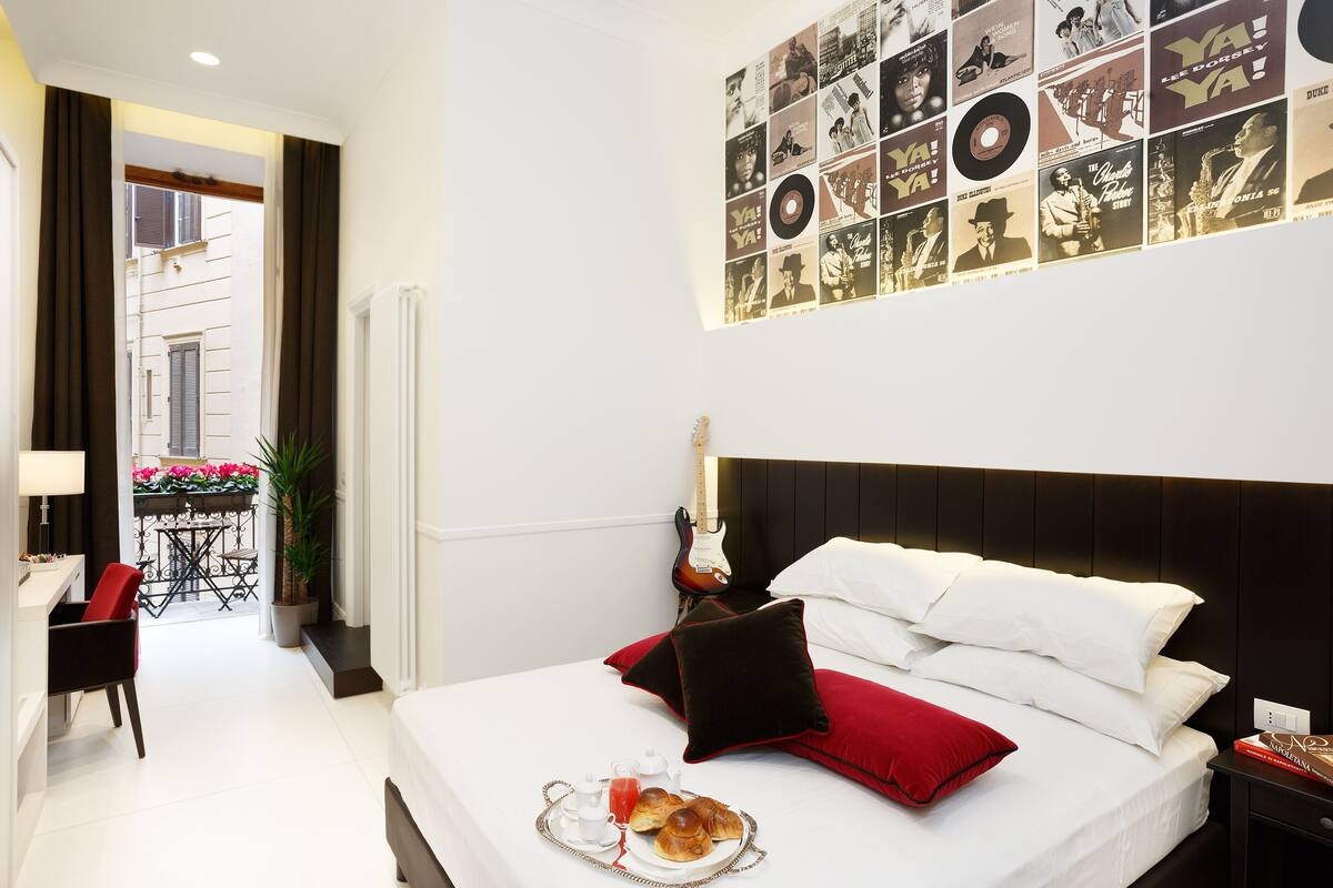 Une chambre d’hôtel avec un lit, une guitare, un plateau de petit-déjeuner et un mur décoré de pochettes d’albums.