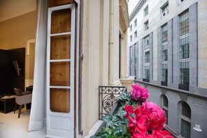 Entrada de hotel con puerta de madera, pared blanca y balcón con flores rosadas.