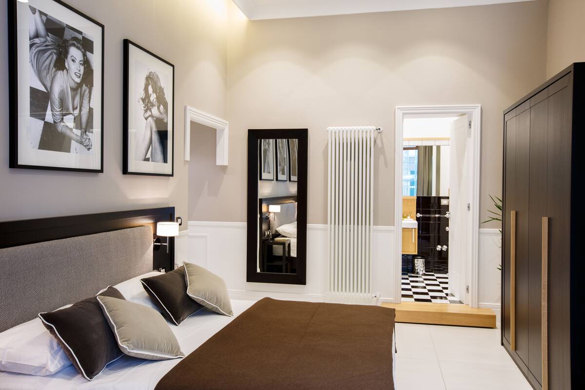 Une chambre d’hôtel avec un lit, une table de chevet, un miroir et des tableaux encadrés au mur.