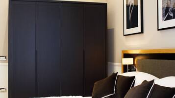 A hotel room with a large dark wardrobe, a bed with white bedding and brown pillows, and a headboard with a lamp.