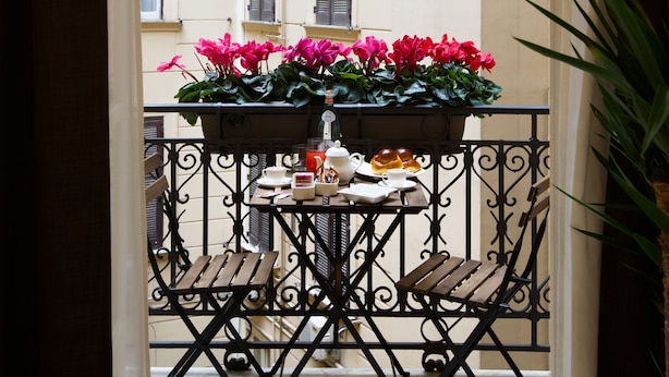 A balcony with a table and chairs, a potted plant, and a view of a building with shutters. - Nap Luxury Guest House (Naples)