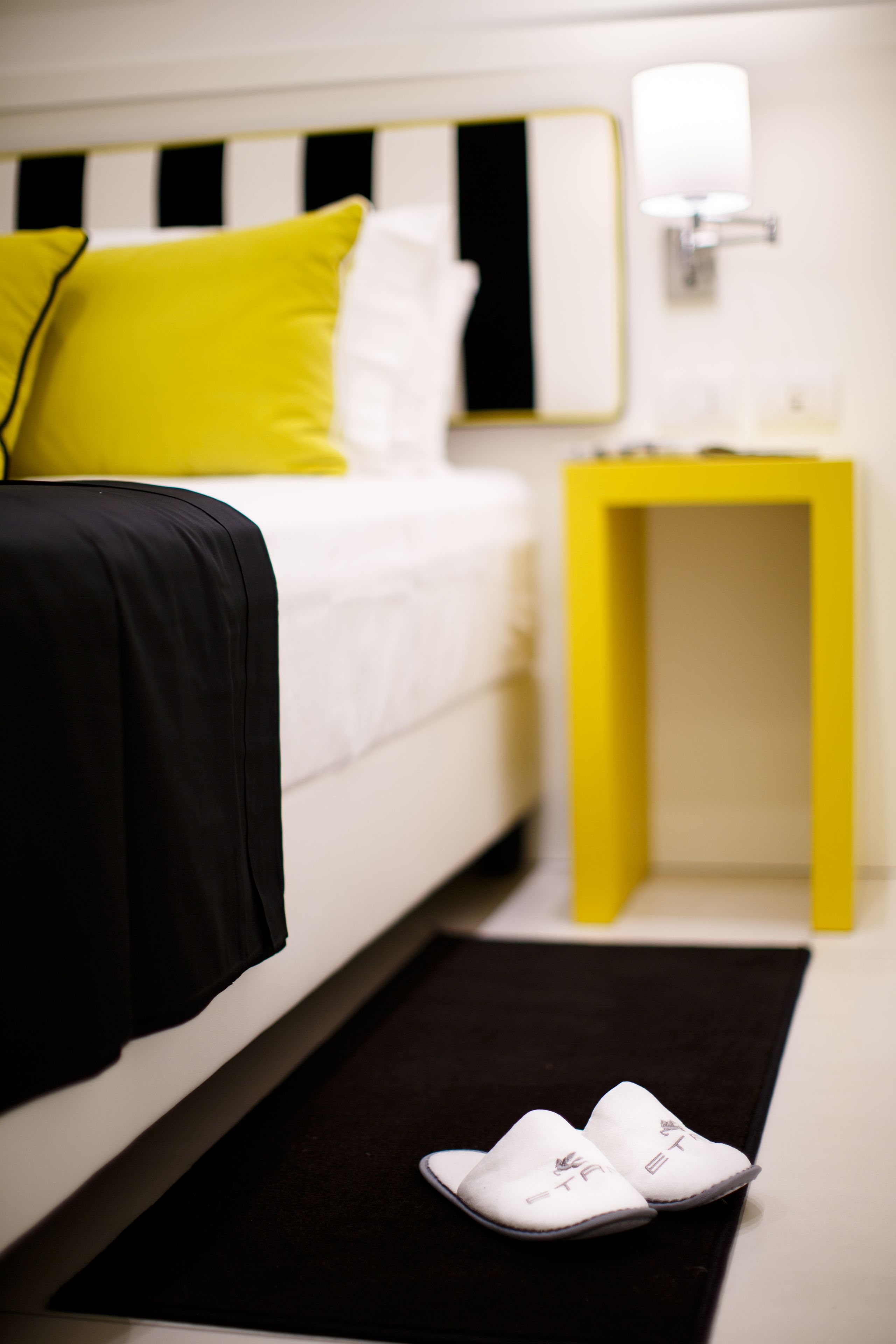 A hotel room with a bed, a nightstand, and a pair of slippers on the floor.