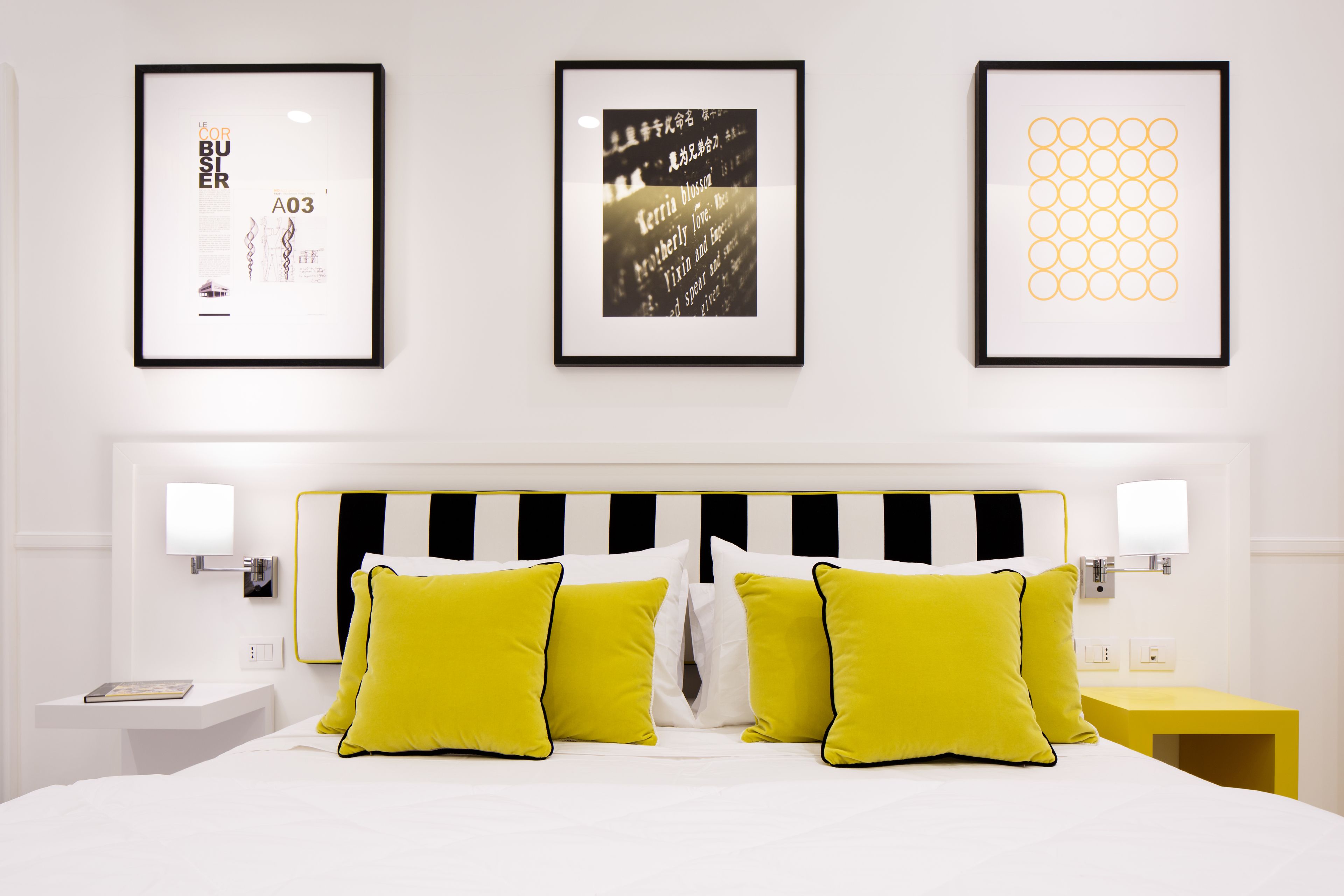 A hotel room with a bed, two bedside tables, and three framed artworks on the wall.