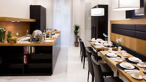 A modern dining area with a long wooden table set for a meal, a kitchen area with a counter, and a seating area with a sofa and chairs. - Nap Luxury Guest House (Naples)