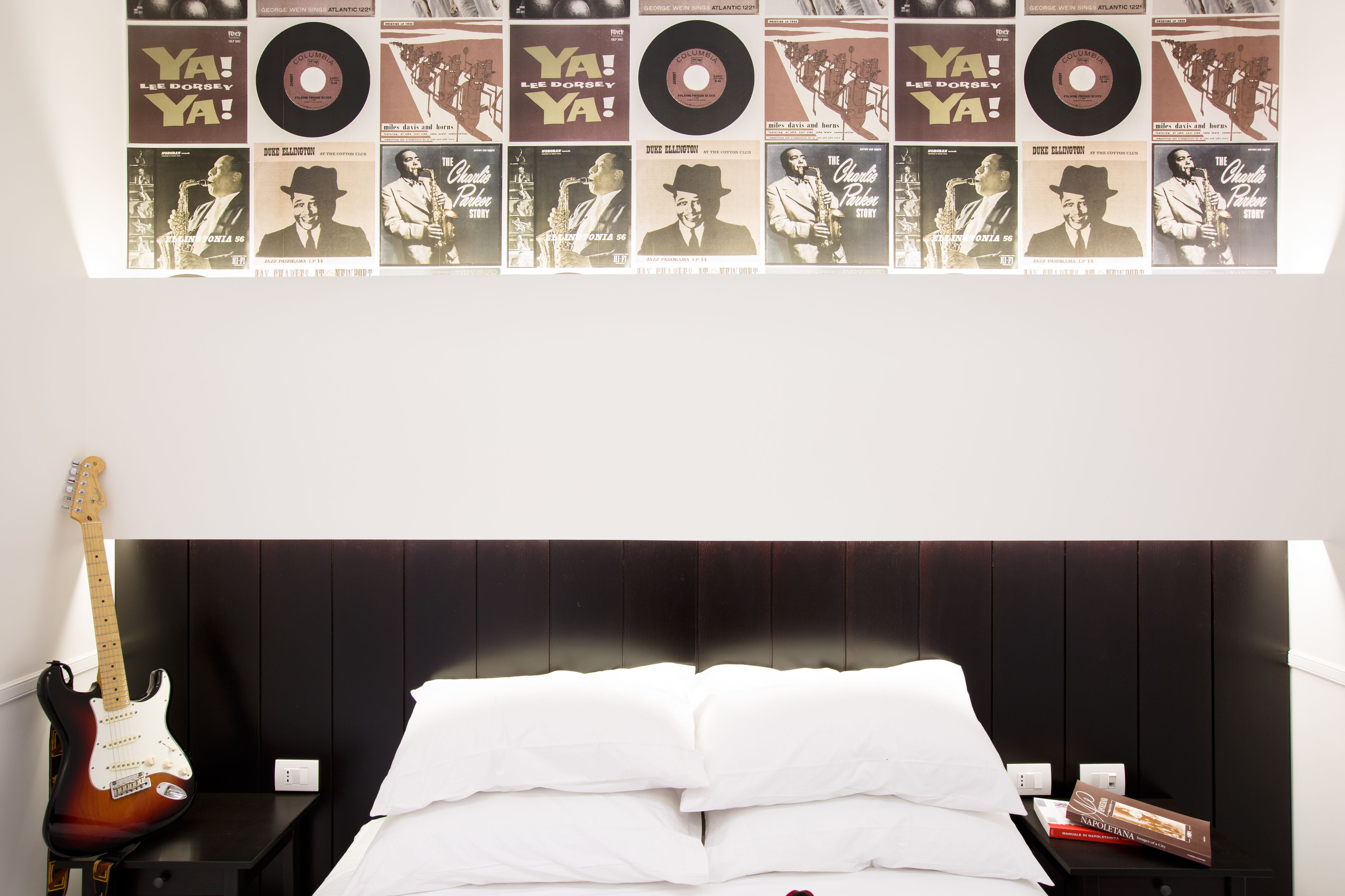 A bedroom with a bed, a guitar, and a wall decorated with vintage album covers.