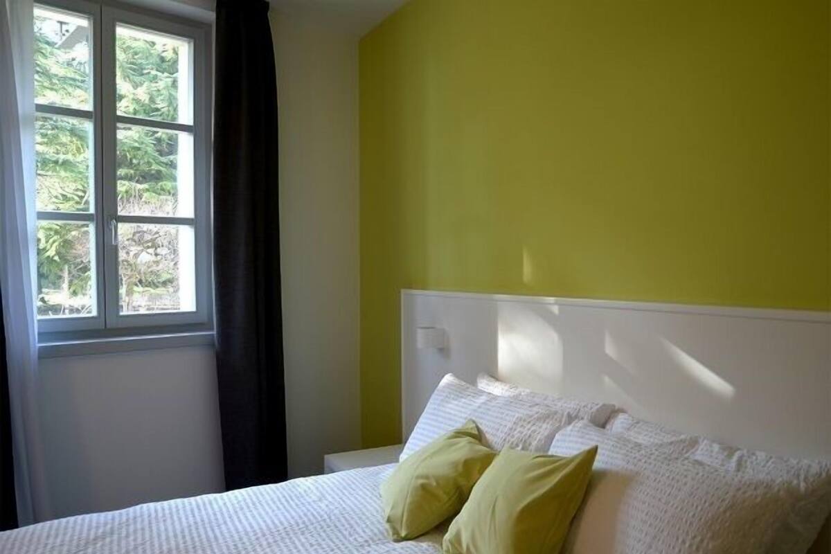 Ein Schlafzimmer mit einem Bett, einem Fenster mit Vorhängen und einer gelben Wand.