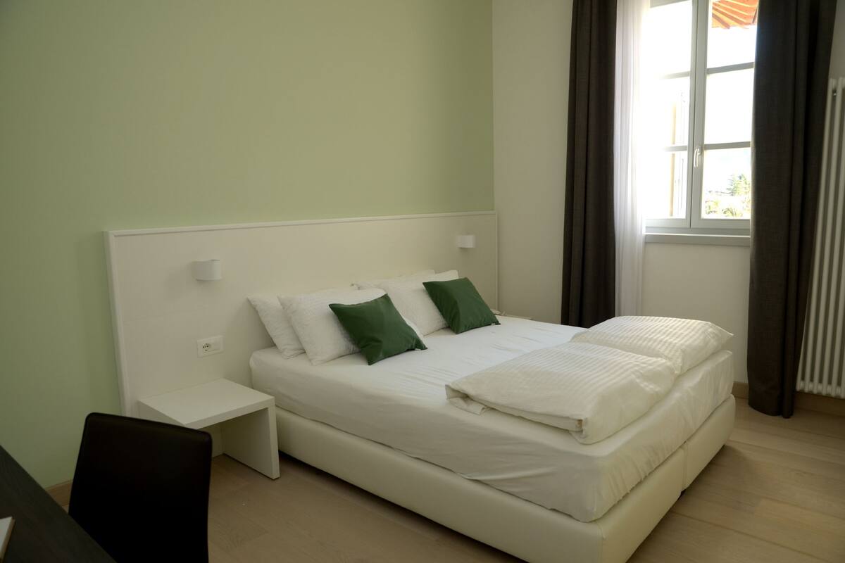 Ein Schlafzimmer mit Bett, Nachttisch und Fenster mit Vorhängen.