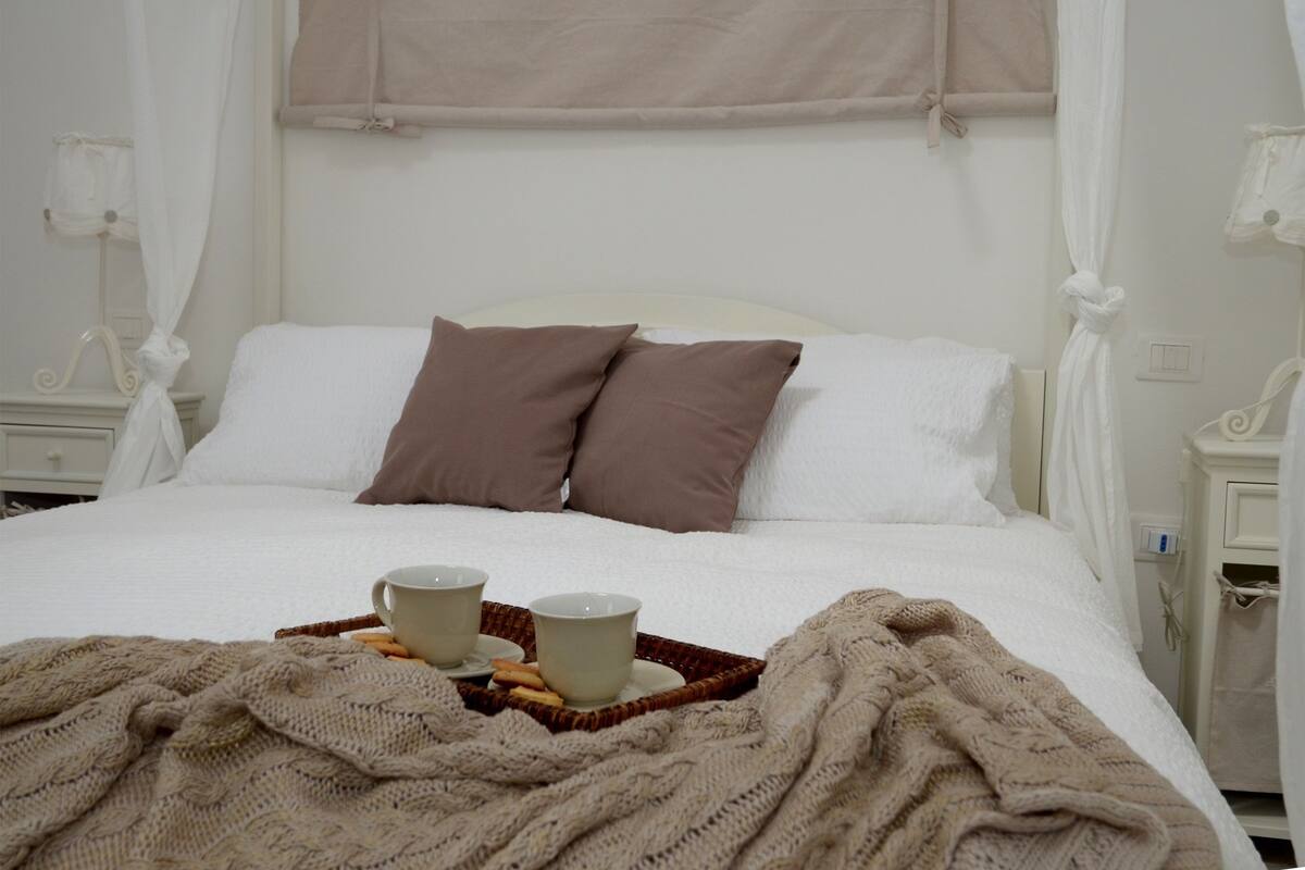 Ein ordentlich bezogenes Bett mit einem weißen Kopfteil, zwei braunen Kissen und einem Tablett mit zwei Tassen und Keksen.