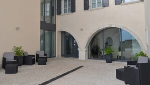 A courtyard with outdoor seating, large windows, and a stone archway. - Borgo San Nazzaro (Riva del Garda)