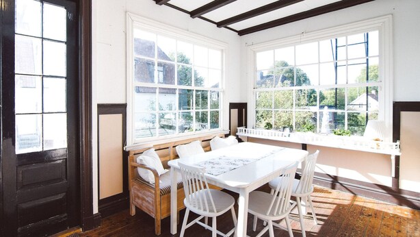 A room with a large window, a wooden bench, a table with chairs, and a door. - Urshult Hotell (Urshult)