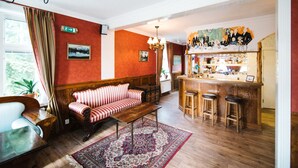 A cozy hotel lobby with a striped sofa, wooden bar stools, a patterned rug, and a bar area with a counter and shelves. - Urshult Hotell (Urshult)