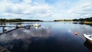 A calm lake with boats docked at a pier, surrounded by trees and a clear sky. - Urshult Hotell (Urshult)