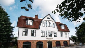 A two-story house with a symmetrical facade, featuring a central entrance with a black door, and a brick base with arched windows. - Urshult Hotell (Urshult)