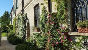 Un bâtiment historique aux murs recouverts de lierre, doté d’une façade en pierre et d’une fenêtre ornée d’une grille en fer forgé.
