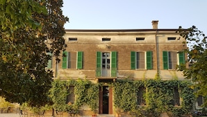 Un bâtiment avec des volets verts, une terrasse en gravier avec des meubles d’extérieur et un jardin.