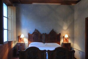 Quarto com uma cama de madeira grande, duas mesas de cabeceira com luminárias e uma janela à esquerda.