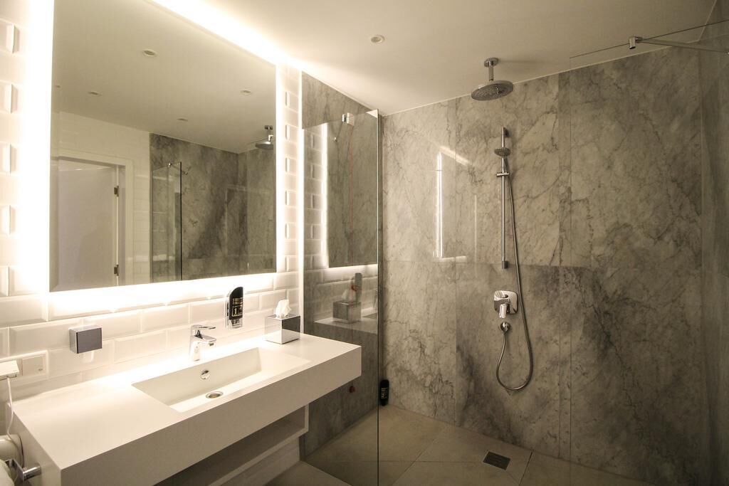 Une salle de bain moderne avec un grand miroir, un lavabo blanc et une douche séparée par des parois en verre.