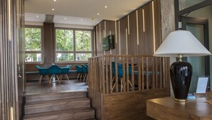 Un moderno vestíbulo de hotel con piso de madera, una escalera, sillas color turquesa y un gran florero sobre una mesa de madera.