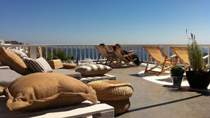 A rooftop terrace with lounge chairs, cushions, and potted plants. - Hotel Porto Carra (Santorini)