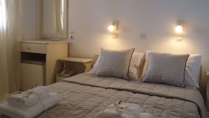 A neatly made bed with two pillows, a bedside table, a mirror, and wall-mounted lights. - Hotel Porto Carra (Santorini)