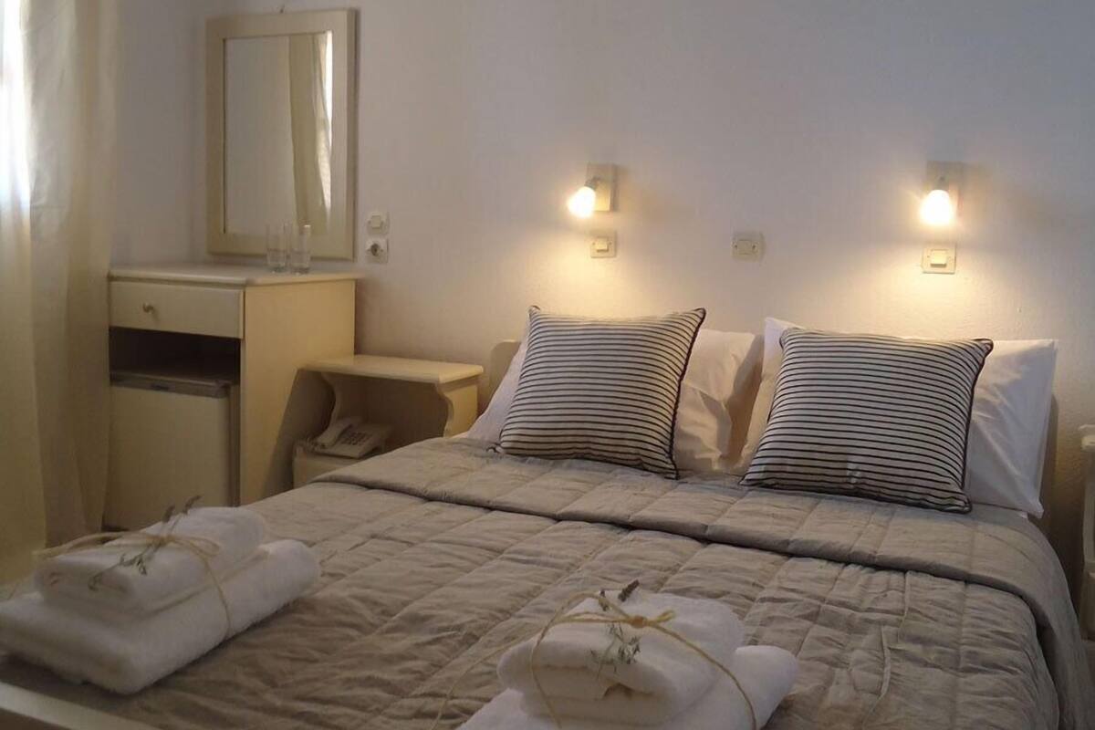 A neatly made bed with two pillows, a bedside table, a mirror, and wall-mounted lights.