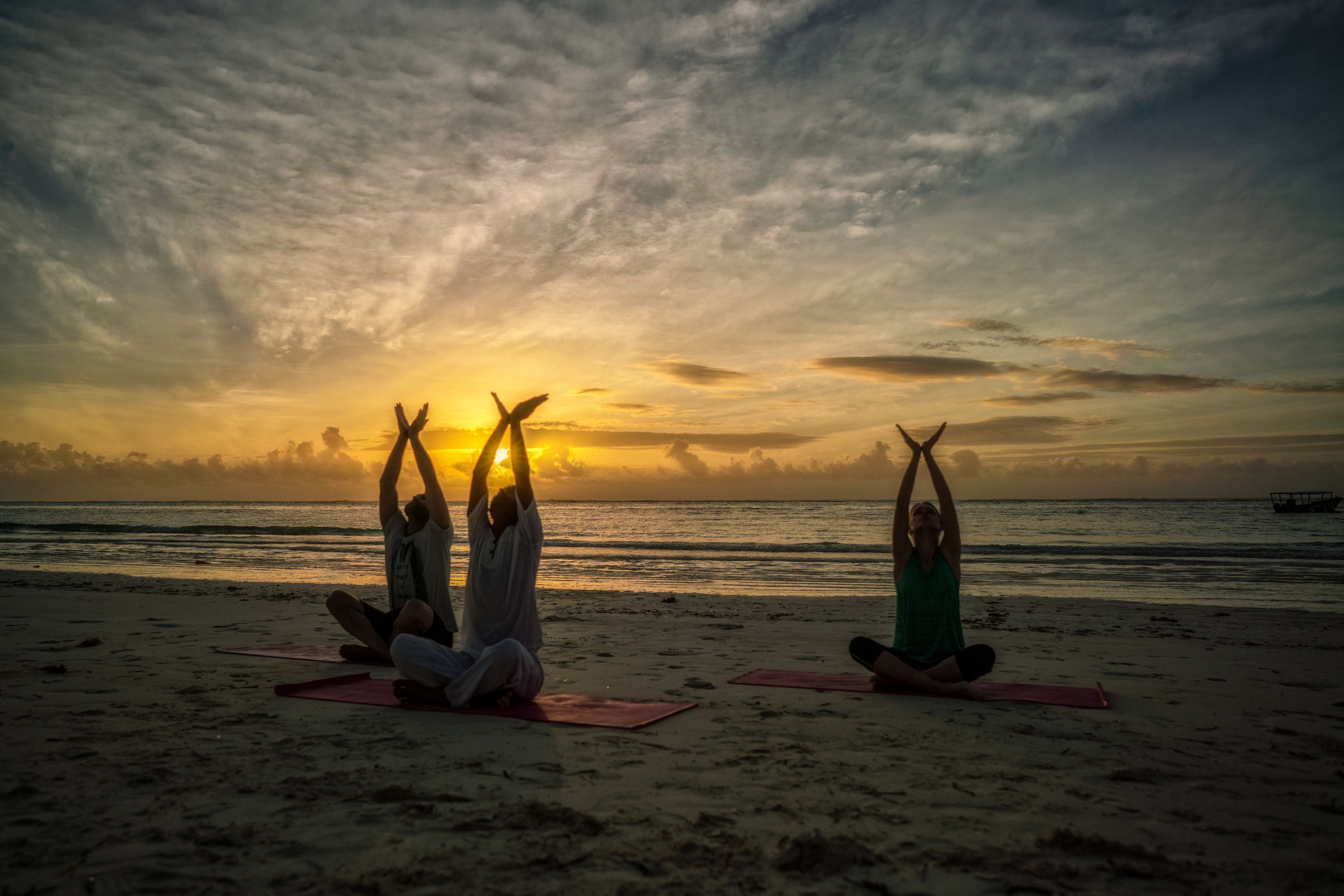 Three people practicing yoga on a beach with a sunset in the background.