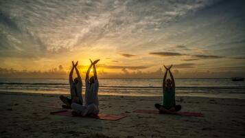 Three people practicing yoga on a beach with a sunset in the background.