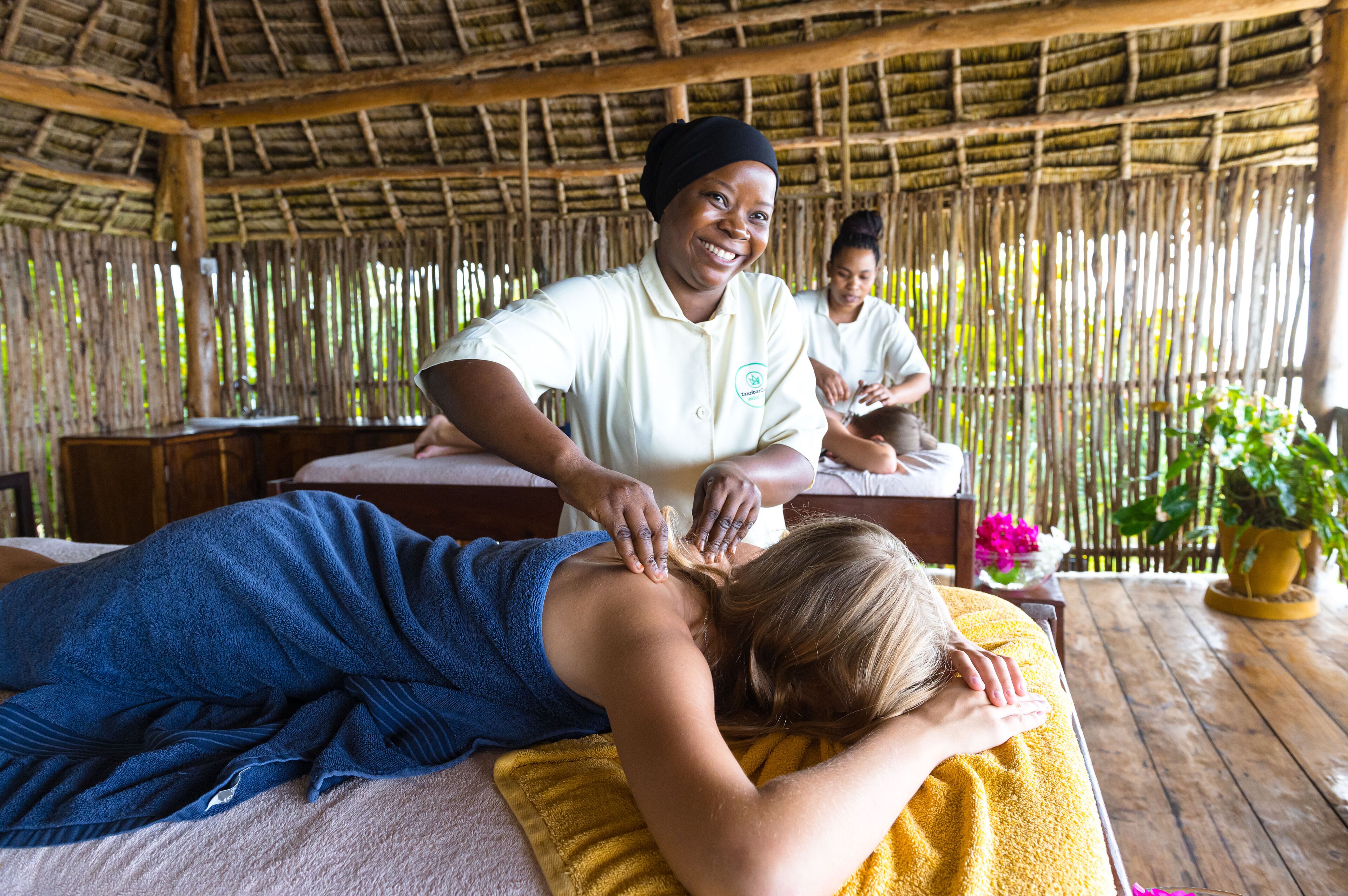 A massage therapy session in a rustic setting with a thatched roof and bamboo walls.