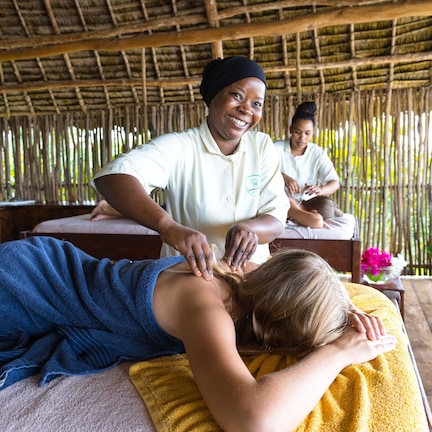 A massage therapy session in a rustic setting with a thatched roof and bamboo walls.
