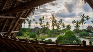 A view from a thatched-roof structure overlooking a beach with palm trees and a cloudy sky. - Zanzibar Queen Hotel (Matemwe)