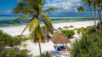 A beach scene with a thatched-roof hut, palm trees, and a clear blue sky.